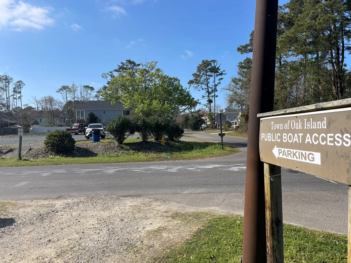 The image shows a parking area near a public boat access point, surrounded by trees and neighboring homes. The scene suggests easy parking for vehicles and trailers and a launch site for boating adventures.