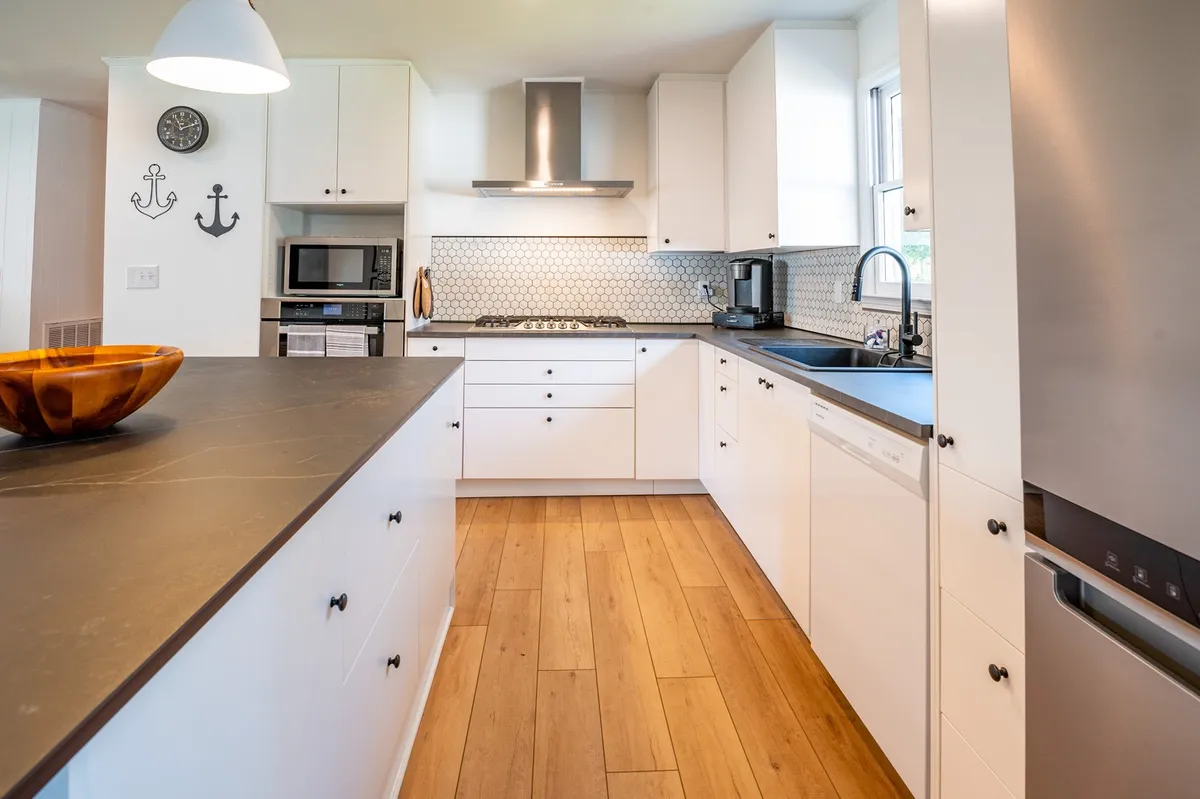 A modern kitchen showcasing a central island with a black countertop, hexagonal backsplash, gleaming white cabinets, and a wooden bowl as a centerpiece. The space is designed for both meal prep and socializing, balancing style and functionality.