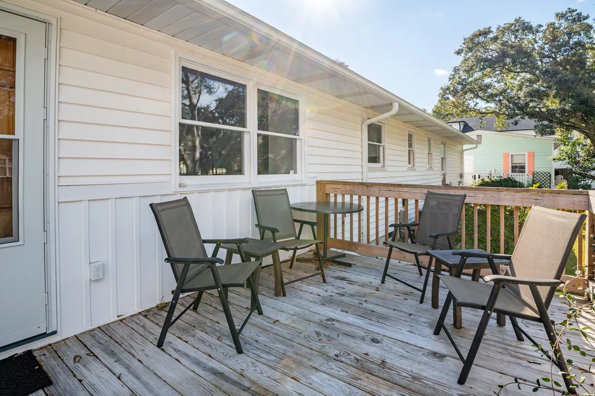 A sunlit wooden deck is set with chairs and a table, creating an inviting spot for relaxation or conversation. The warm glow hints at sunset moments or post-beach unwinding, with ample seating for small group gatherings.