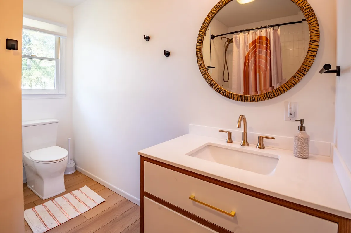 A tranquil bathroom scene featuring a round mirror above the sink and a shower with a curtain, all in a soothing, minimalist design. The space feels inviting and practical for guests or family use.