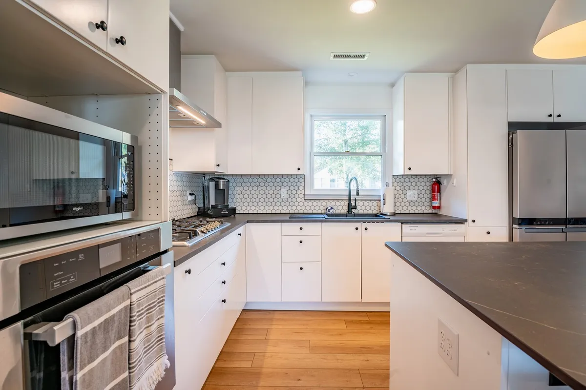 A bright, functional kitchen with stainless steel appliances, a hexagonal tile backsplash, and a large kitchen island. The space is well-lit and perfect for family gatherings or casual meals.